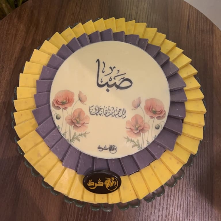 صينية مولودة بمراوح شوكولاتة صفراء وبنفسجية حول قرص كبير مرسوم عليه زهور الخشخاش
